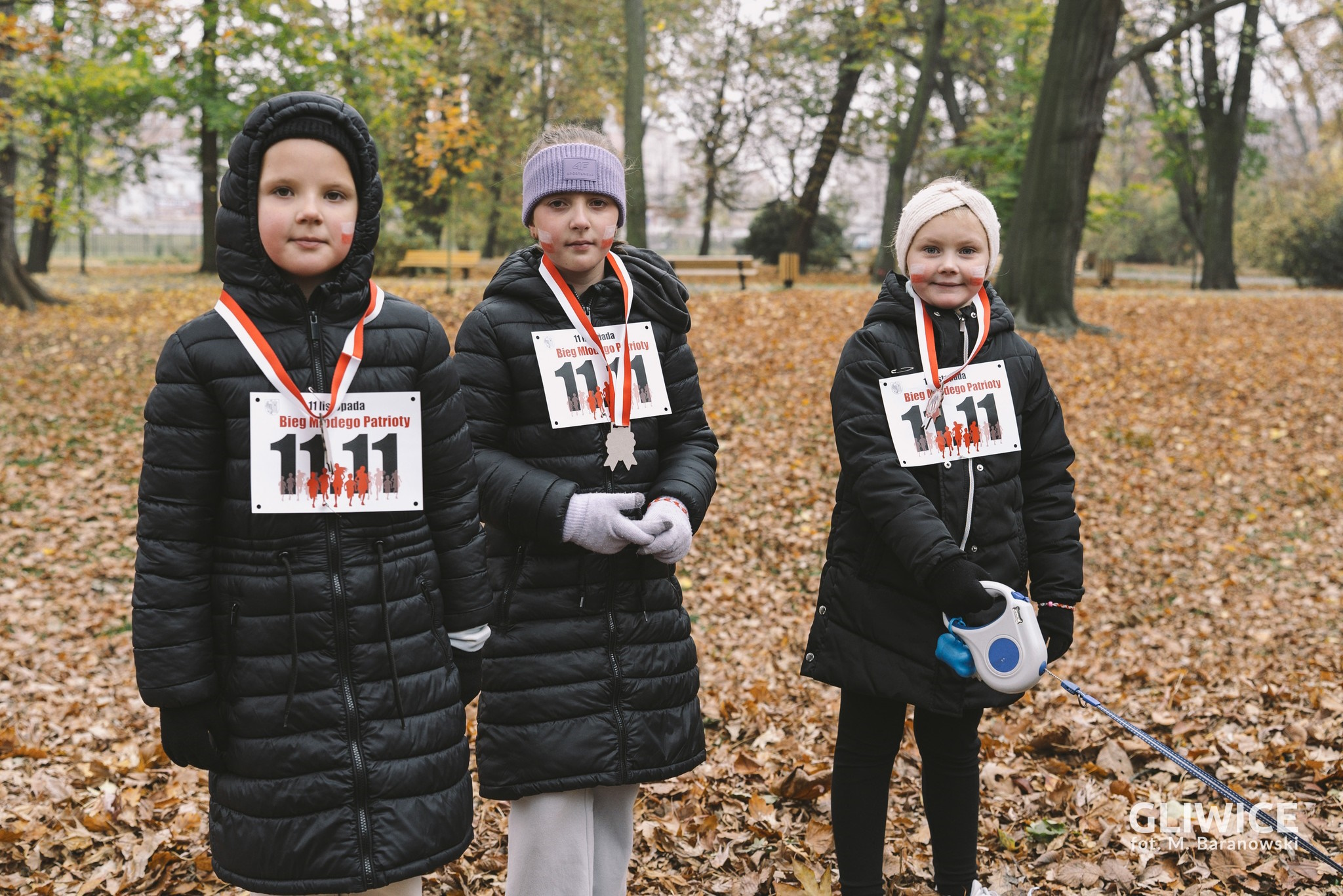 Trzy dziewczynki z medalami i numerami startowymi w parku