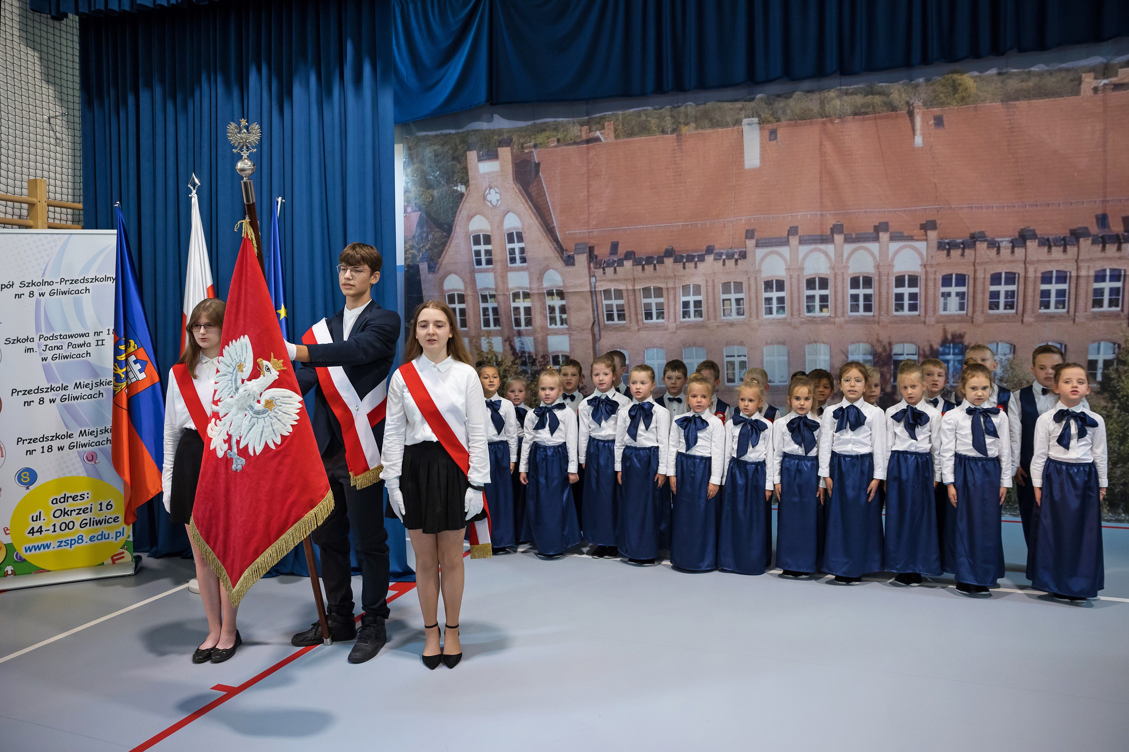 Ubrani na galowo uczniowie, stojący na baczność i trzymający sztandar szkoły