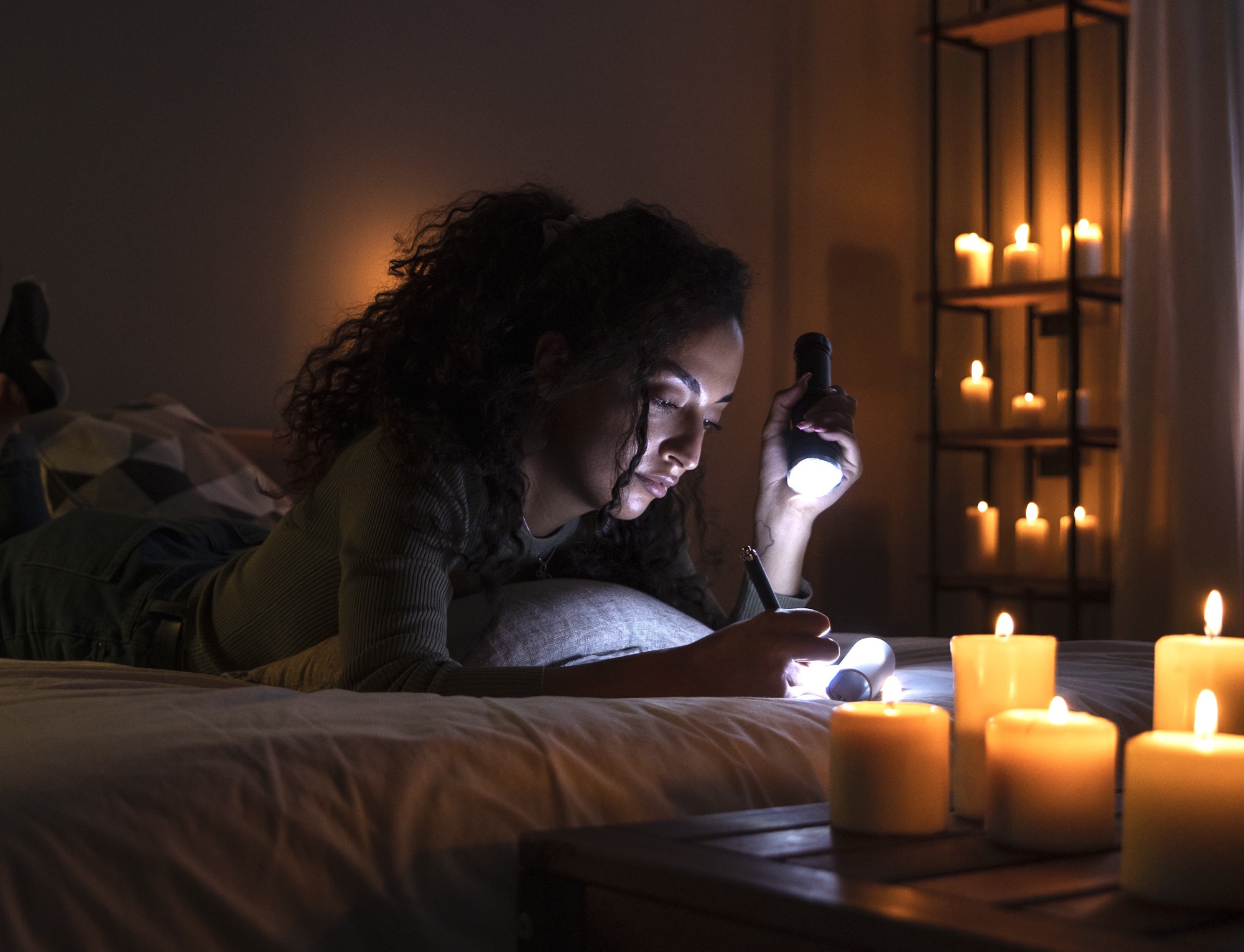 kobieta zapisuje notatki podczas awarii światła, korzystając z latarki i rozstawionych dookoła świec