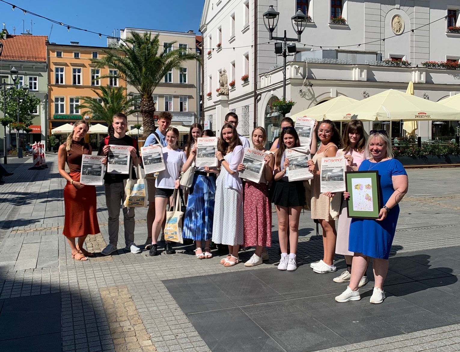 Uczniowie i koordynatorki projektu trzymający wydanie Nowin Gliwickich na tle Ratusza